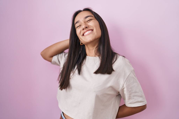 Young hispanic woman standing over pink background stretching back, tired and relaxed, sleepy and yawning for early morning  - Photo, Image