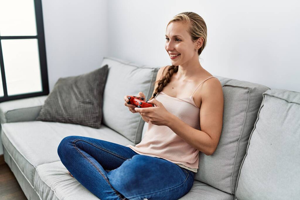 Νεαρή καυκάσια γυναίκα που παίζει βιντεοπαιχνίδι καθισμένη στον καναπέ στο σπίτι - Φωτογραφία, εικόνα