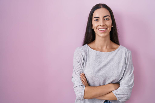 Young brunette woman standing over pink background happy face smiling with crossed arms looking at the camera. positive person.  - Photo, Image