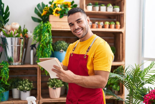 Young hispanic man florist smiling confident writing on notebook at florist - Photo, Image