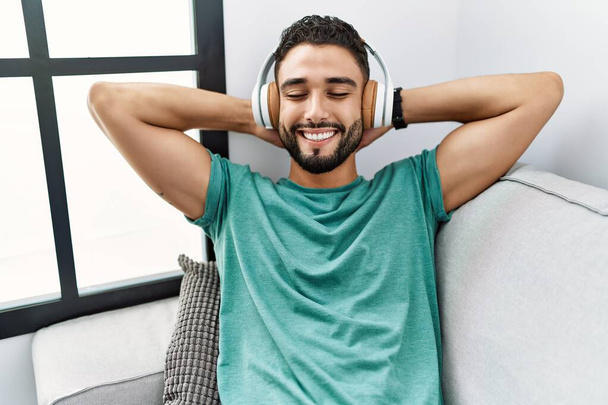 Jovem árabe homem ouvindo música sentado no sofá em casa - Foto, Imagem