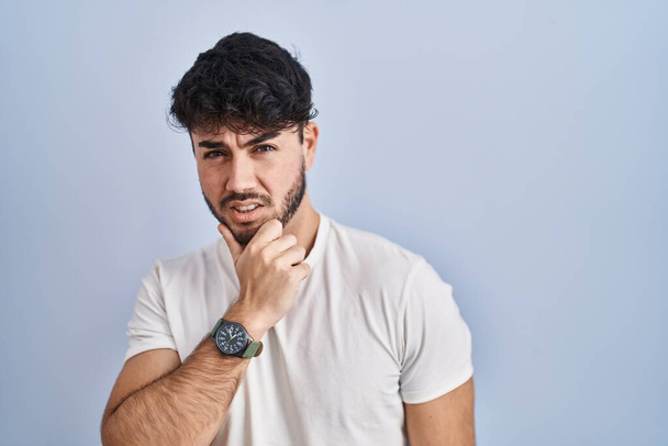 Hispanic man with beard standing over white background thinking worried about a question, concerned and nervous with hand on chin  - Foto, Imagem