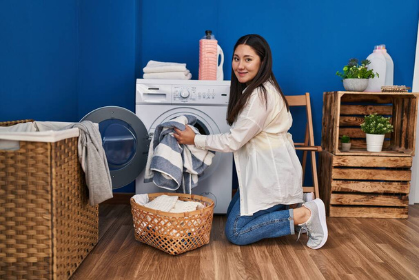 Young hispanic woman smiling confident washing clothes at laundry room - Foto, imagen