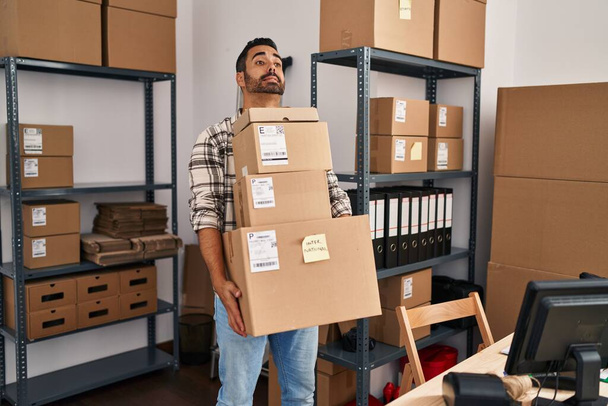 Mladý hispánec muž ekommerce obchodní pracovník držící balíčky v kanceláři - Fotografie, Obrázek