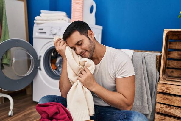 Young hispanic man touching face with soft clothes at laundry room - Photo, Image