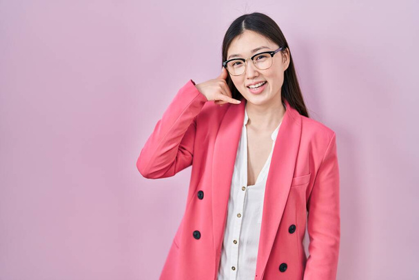 Jovem empresária chinesa usando óculos sorrindo fazendo gesto de telefone com a mão e os dedos como falar ao telefone. conceitos comunicantes.  - Foto, Imagem