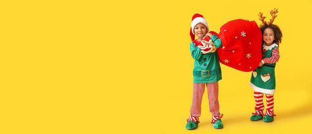 Sarı arka planda Noel Baba çantası tutan şirin küçük elfler ve mesaj için yer var. - Fotoğraf, Görsel
