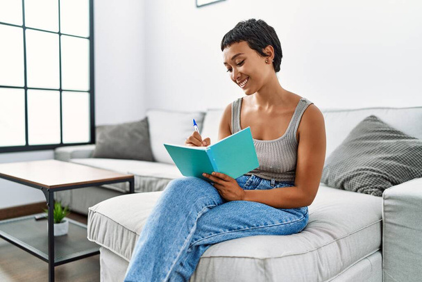 Young hispanic woman smiling confident writing on notebook at home - Photo, Image