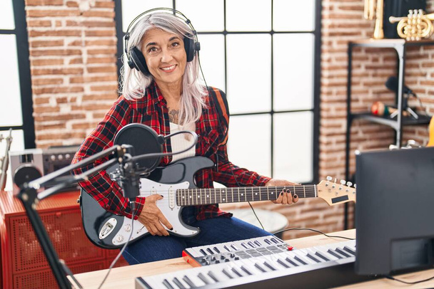 Μέση ηλικία γκρίζα μαλλιά γυναίκα μουσικός παίζει ηλεκτρική κιθάρα στο στούντιο μουσικής - Φωτογραφία, εικόνα