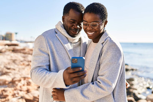 Man and woman couple standing together using smartphone at seaside - Фото, зображення
