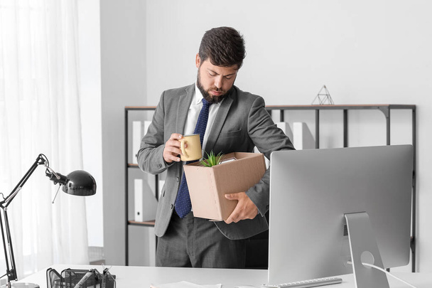 Уволенный молодой человек держит коробку со своими вещами в офисе - Фото, изображение