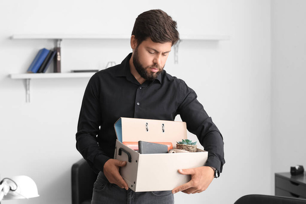 Fired young man holding box with personal stuff in office - Foto, Imagen