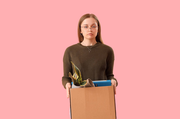 Fired young woman holding box with personal stuff on pink background - Photo, Image