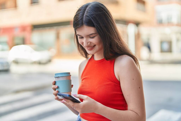 Mladý kavkazský žena pomocí smartphone pití kávy na ulici - Fotografie, Obrázek