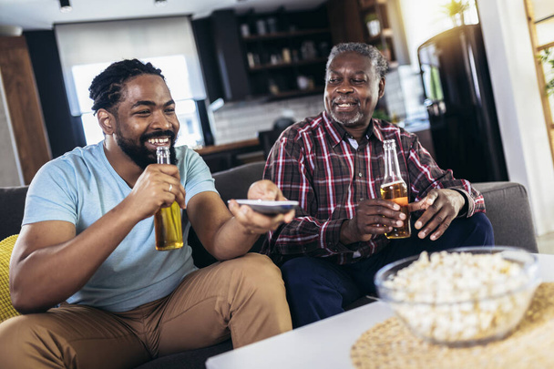 Emocionado viejo padre e hijo viendo la televisión, beber cerveza, divertirse en casa - Foto, imagen