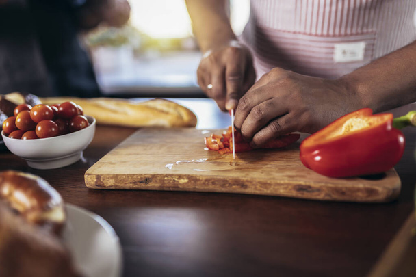 Man cooking in apron cut red pepper on wood board concept against kitchen background - Photo, Image