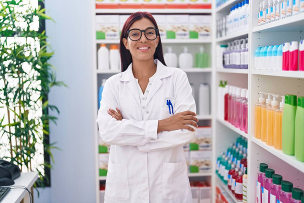 Young beautiful hispanic woman pharmacist smiling confident standing with arms crossed gesture at pharmacy - Foto, imagen