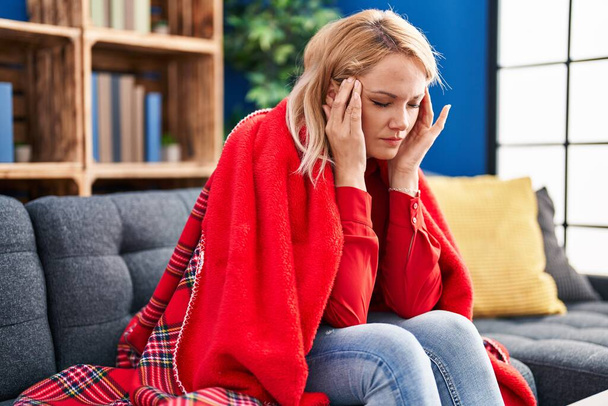 Nuori blondi nainen kärsii päänsärky istuu sohvalla kotona - Valokuva, kuva