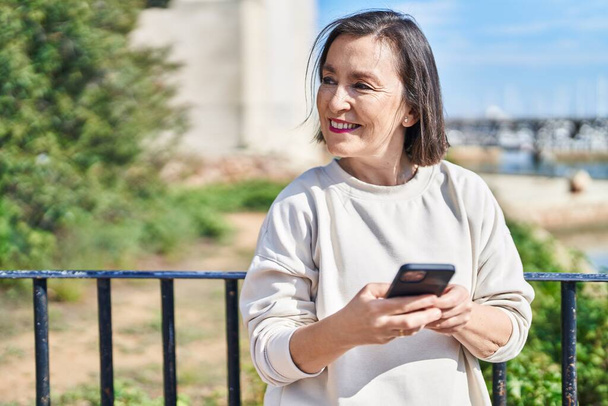 Middle age woman smiling confident using smartphone at seaside - Foto, Imagen