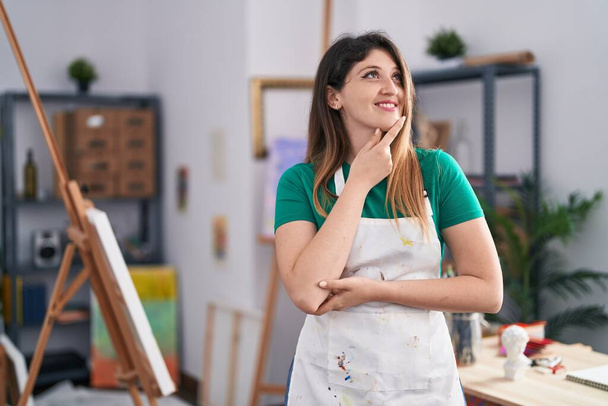 Young brunette woman at art studio smiling looking confident at the camera with crossed arms and hand on chin. thinking positive.  - Foto, Imagen