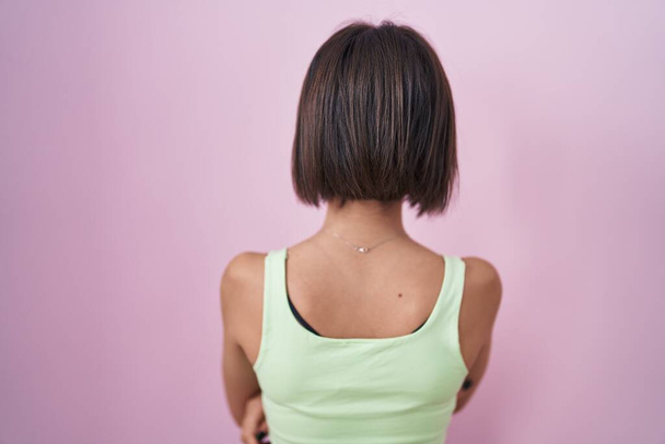 Молодая девушка, стоящая на розовом фоне, смотрит назад, скрестив руки.  - Фото, изображение