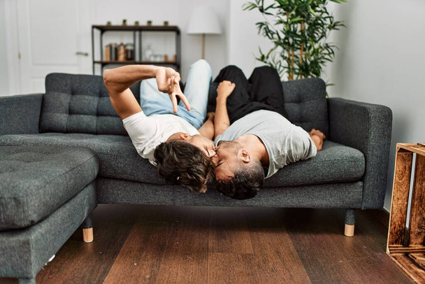 Two hispanic men couple kissing and lying on sofa at home - Fotografie, Obrázek