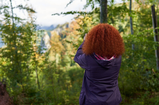 Redhead woman with curly hair and camera hiking on a trail in the mountain forest - Fotografie, Obrázek