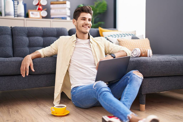Jonge Spaanse man met laptop op de vloer thuis - Foto, afbeelding