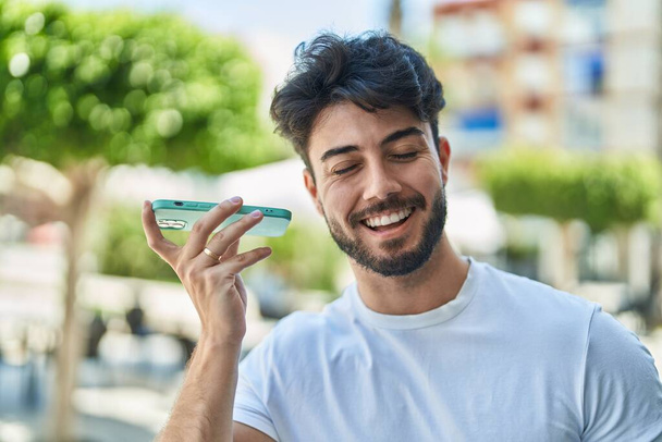 Młody Latynos uśmiecha się pewnie słuchając wiadomości dźwiękowych ze smartfona na ulicy - Zdjęcie, obraz