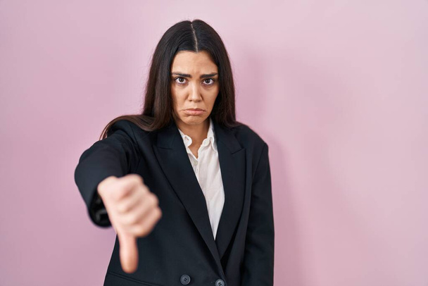 Young brunette woman wearing business style over pink background looking unhappy and angry showing rejection and negative with thumbs down gesture. bad expression.  - Photo, Image