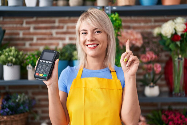 Young caucasian woman working at florist shop holding dataphone surprised with an idea or question pointing finger with happy face, number one  - Photo, Image
