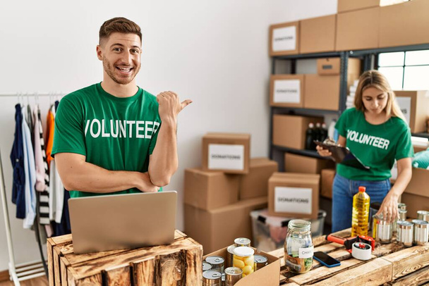 Молодой человек и женщина в футболке добровольца на пожертвования стоят улыбаясь счастливо указывая рукой и пальцем в сторону  - Фото, изображение
