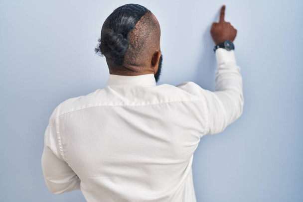 Afro-Américain debout sur fond bleu posant vers l'arrière pointant vers l'avant avec la main du doigt  - Photo, image