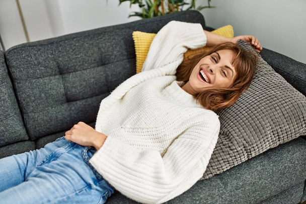 Nuori valkoihoinen nainen hymyilee luottavainen makaa sohvalla kotona - Valokuva, kuva