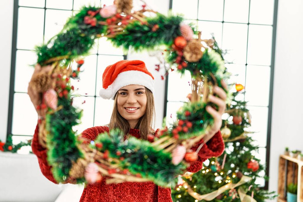 Молода іспаномовна дівчина посміхається щасливий тримає різдвяний декор вдома
. - Фото, зображення