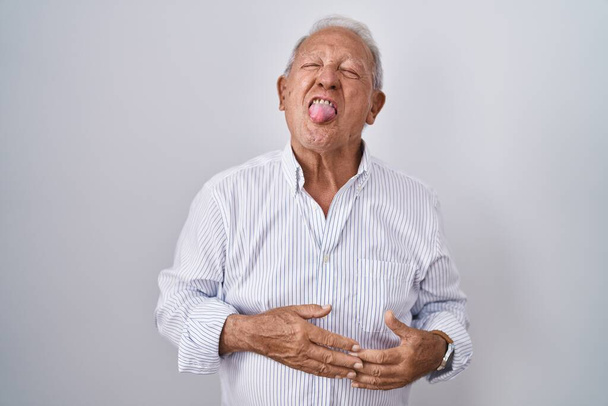 Senior man with grey hair standing over isolated background sticking tongue out happy with funny expression. emotion concept.  - Photo, Image