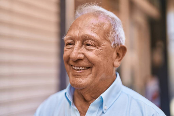 Homme âgé aux cheveux gris souriant confiant debout dans la rue - Photo, image