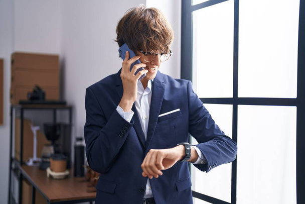 Jonge blonde man zakelijke werknemer praten op smartphone kijken horloge op kantoor - Foto, afbeelding