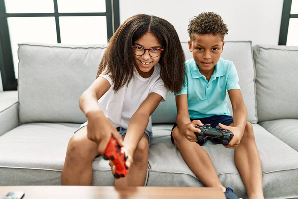 Veli ja sisko pelaa videopeliä istuu sohvalla kotona - Valokuva, kuva