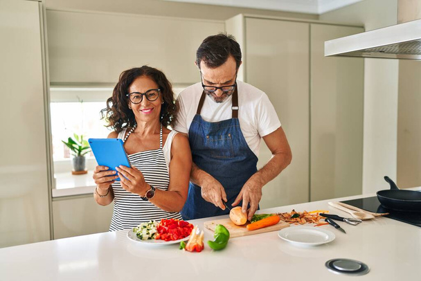 Moyen âge couple hispanique souriant cuisine confiante et en utilisant touchpad à la cuisine - Photo, image