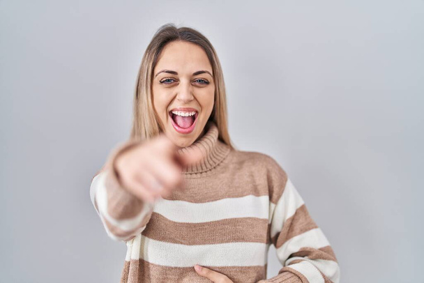 Νεαρή ξανθιά γυναίκα φορώντας ζιβάγκο πουλόβερ πάνω από απομονωμένη φόντο γέλιο σε σας, δείχνοντας το δάχτυλο στην κάμερα με το χέρι πάνω από το σώμα, έκφραση ντροπή  - Φωτογραφία, εικόνα