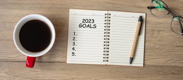 2023 GOAL with notebook, black coffee cup and pen on wood table, Top view and copy space. Happy New Year, Resolution, To do list, Strategy and Plan concept - 写真・画像
