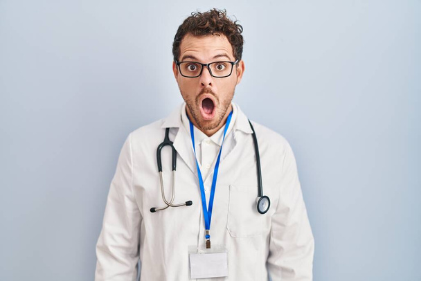 Young hispanic man wearing doctor uniform and stethoscope afraid and shocked with surprise expression, fear and excited face.  - Fotografie, Obrázek
