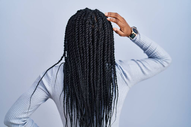 Afrikkalainen amerikkalainen nainen seisoo sinisellä taustalla taaksepäin ajatellen epäilystä käsi pään päällä  - Valokuva, kuva