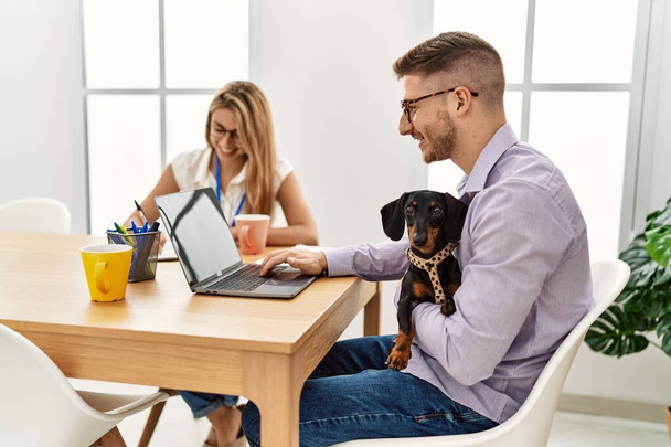Двое бизнесменов улыбаются счастливой работе с собакой в офисе. - Фото, изображение