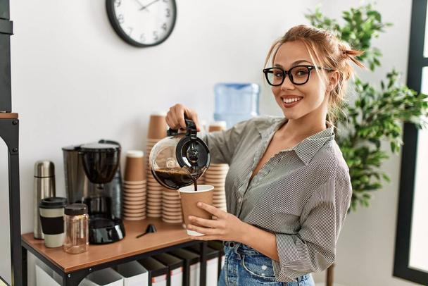 Jonge blanke vrouw zakenman gieten koffie op afhaalglas op kantoor - Foto, afbeelding