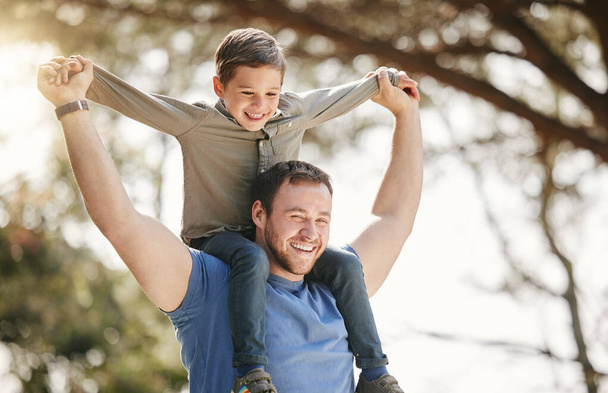 Happy caucasian father and son having fun and playing together outside. Carefree man carrying excited son on his shoulders while bonding in at the park. Single dad enjoying quality time with kid. - Valokuva, kuva