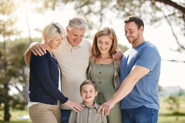 Portrait of a smiling multi generation caucasian family standing close together outdoors. Adorable little boy bonding with his mother, father, grandfather and grandmother at a park. Family putting th. - Photo, image