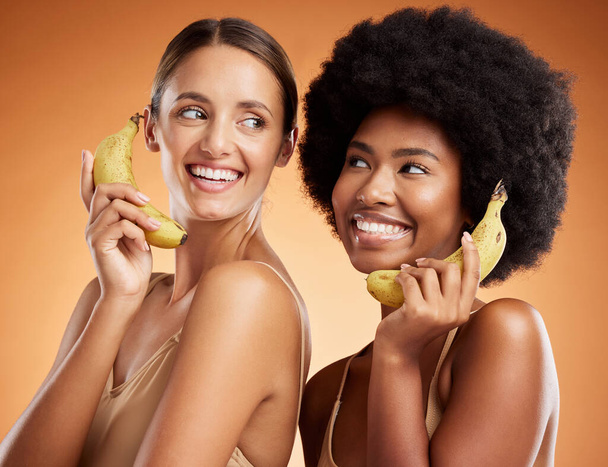 Beauty, diversity and women on banana phone, black woman and friend act, smile and fun pretending to be on phone call. Playful, friendship and studio portrait of happy girls with fruit and fake chat - Fotó, kép