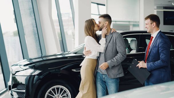 Young bearded man is buying car for his attractive wife, she is kissing and hugging him. - Foto, Imagem